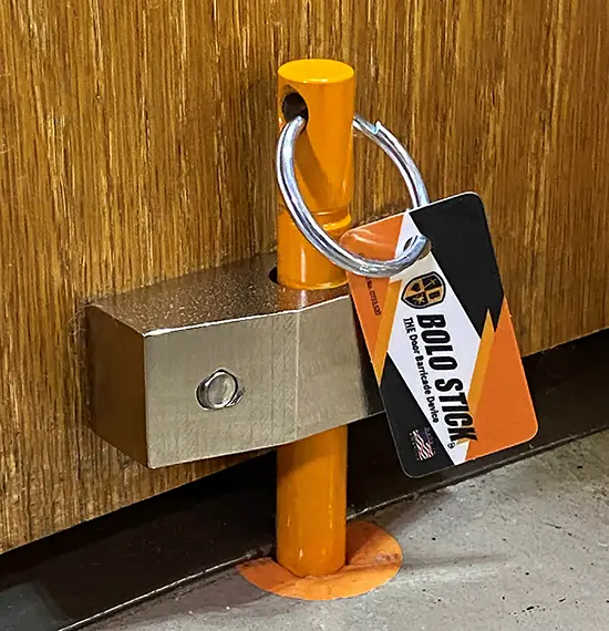 Bolo Stick pin with its orange key tag set in the steel bracket at the base of a wooden door